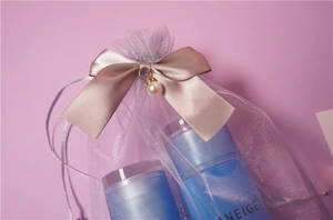 Close-up of purple organza gift bag with pink bow, pearl pendant and cosmetics