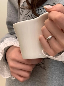 Detail of s925 silver smiley face open ring worn on finger holding a white mug