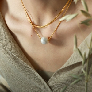 Double-layered gold blade chain necklace with a white pearl pendant worn by a model