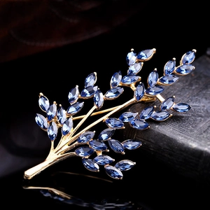 Close-up of golden wheat brooch with blue crystal leaves on a black reflective surface