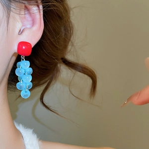 Detail of square red resin earrings with blue grape tassel worn by model in soft light