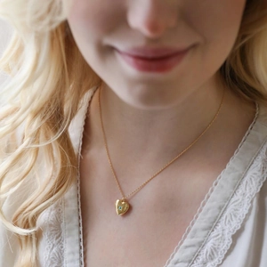 Golden heart locket necklace with turquoise gemstone and starburst engraving on model