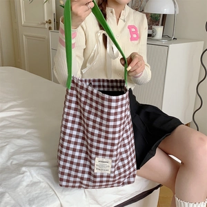 Détail du sac cabas en toile à carreaux avec anses vertes et écusson de marque en chambre