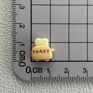 Macro shot of miniature yellow resin toaster accessory measuring 1.5cm on a grid mat