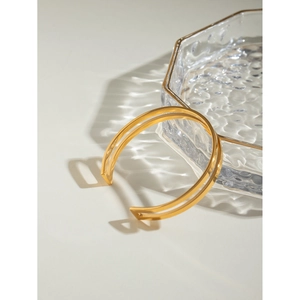 Macro view of 18k gold plated stainless steel open bangle on a glass tray