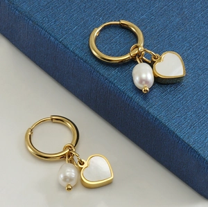 Détail de boucles d'oreilles créoles dorées 18K avec pendentif cœur et perle blanche