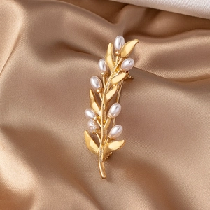 Elegant gold leaf branch brooch with white pearls over champagne satin background