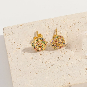 Detail of gold flower earrings with colorful zircon stones on a beige stone surface