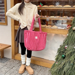 Détail du sac cabas en peluche rayé rouge et rose avec étiquette dans une boulangerie