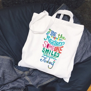 Minimalist white canvas tote bag with colorful letter print on denim background