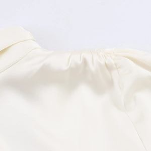 Detail view of smooth off-white satin fabric with elegant shoulder pleats and ruffles