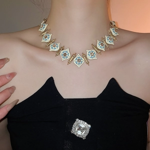Detail of white enamel necklace with blue floral patterns and gold-tone metal accents