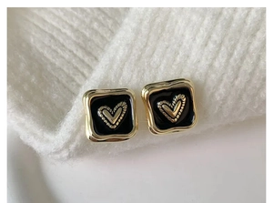 Vista dettagliata di orecchini quadrati in oro con smalto nero e cuore su maglia bianca