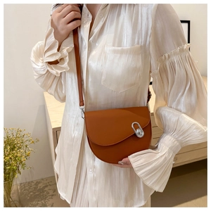 Detailed shot of a brown leather saddle bag with silver buckle worn by a model