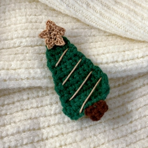 Close-up of a handmade crochet green Christmas tree hairpin on a soft knit fabric