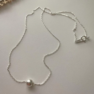 Detailed view of an 8mm polished silver bead pendant on a delicate cross chain