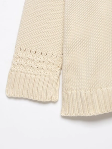 Detail of off-white knit cardigan showing hollow geometric patterns and ribbed cuffs