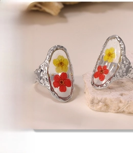 Close-up of stainless steel resin rings with colorful dried flowers on a stone base