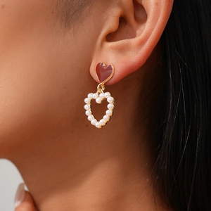 Detail view of red heart and faux pearl drop earrings on a model for elegant styling