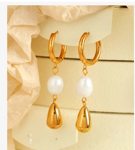 Dettaglio macro di orecchini vintage in oro con perle e pendente a goccia su sfondo beige