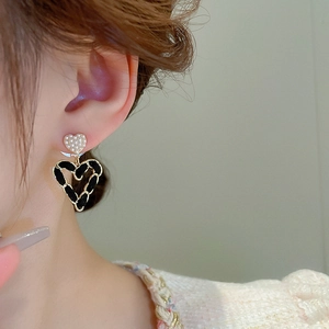 Close-up of heart earrings with woven black leather chain and delicate pearl studs