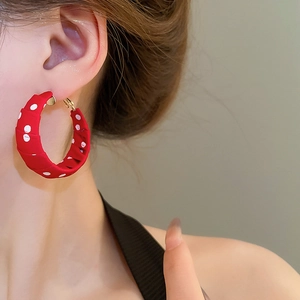 Close-up of a model wearing large red fabric earrings with white polka dots