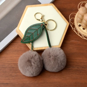 Close-up of brown faux fur cherry keychain with green leather leaf and golden metal hardware