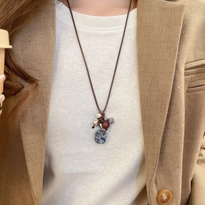 Ethnic style necklace detail with blue spotted stone and metal charms on a wax cord