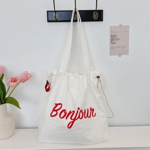 Detail of white canvas drawstring bag with red Bonjour lettering on a wall hook
