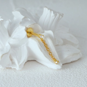Detail of gold cartilage stud featuring a dual-stone chain drop on a ceramic background