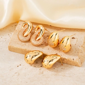 Three pairs of elegant gold vintage earrings with cubic zirconia on a stone surface
