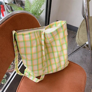 Detail view of a green and yellow plaid canvas tote bag resting on an orange chair