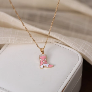 Macro view of a pink enamel cowboy boot pendant with stars on a gold twisted chain