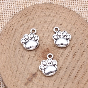 Three silver metal dog paw charms for DIY necklaces on a wooden coaster background