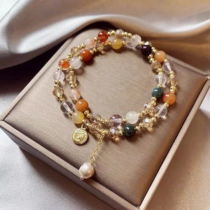 Close-up of multi-layer beaded bracelet with gold coin charm and drop pearl detail