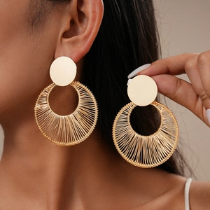 Detail of gold metal wire-wrapped circular earrings shown on model and held by hand