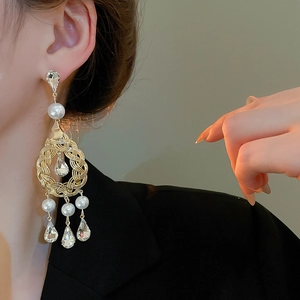 Macro detail of ornate gold teardrop earrings with crystals and white pearls