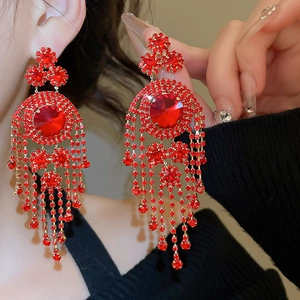 Detail shot of elegant red crystal earrings with long gold tassel and geometric circular studs