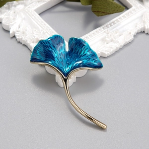 Macro detail of peacock blue enamel ginkgo leaf brooch with golden metal textures