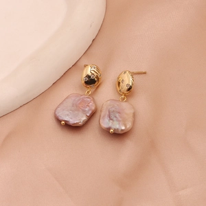 Detailed close-up of Baroque pearl earrings with sparkling crystals on pink satin