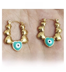 Close-up of golden heart hoop earrings featuring turquoise evil eye charms on palm