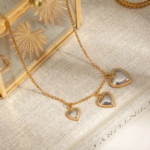 Close-up of golden chain necklace with three silver heart pendants and gold beaded edges