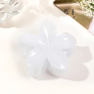 Detailed close-up of a glossy white flower hair claw clip on elegant fabric and magazine