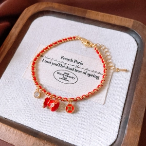 Detail of red woven bracelet with 18k gold lucky pouch and coin pendants