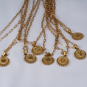 Macro view of gold paperclip chain necklace with initial round coin pendant