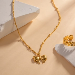 Detailed view of 18K gold plated butterfly necklace and leaf ring on decorative stone