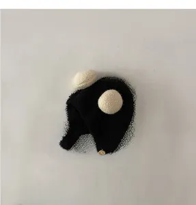 Close-up of black plush baby earflap hat with cream pom-poms and a wooden button detail
