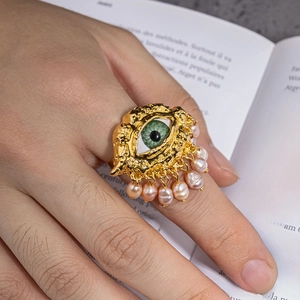 Detailed shot of an evil eye ring with green eye and pink pearl tassels worn on hand