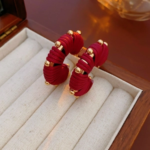 Macro shot of red woven C-shaped earrings with gold beads in a white velvet jewelry box
