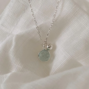 Detailed view of sterling silver necklace with light blue round crystal on white linen
